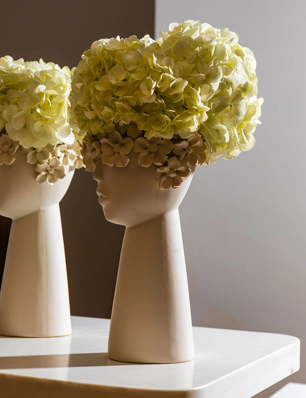 Two sculpted vases holding pale green hydrangeas