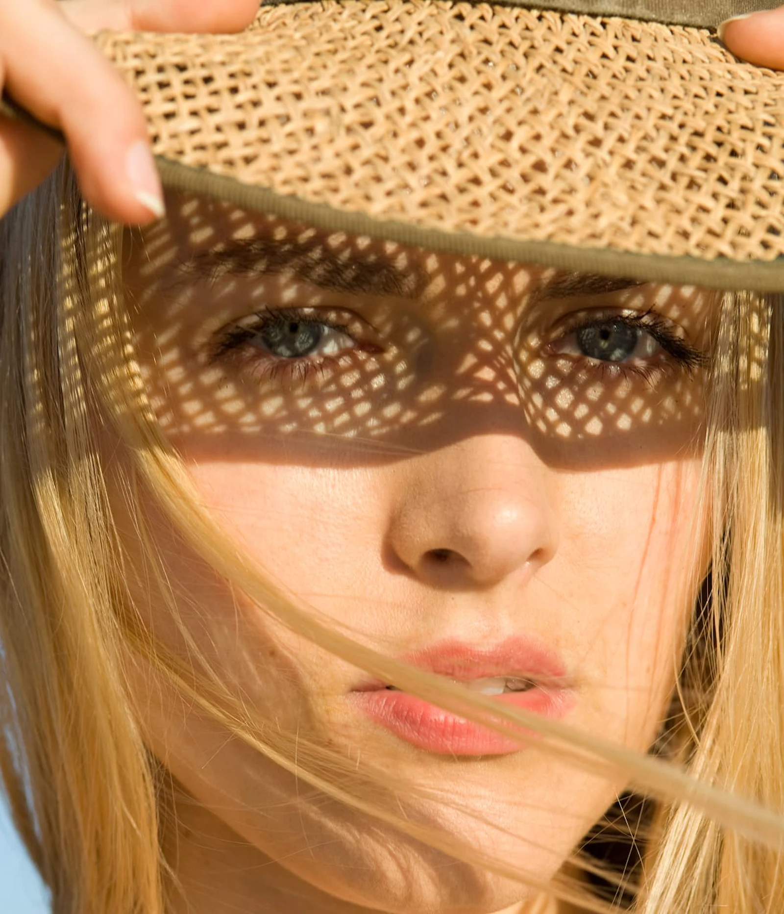 Woman shading her face with a woven sun hat